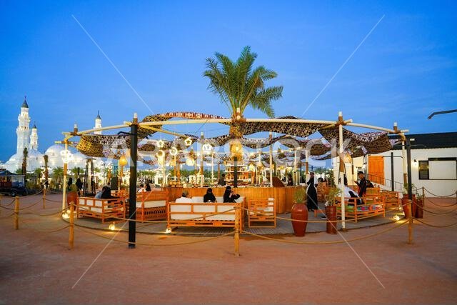 Traditional open-air cafe decorated with illuminated crescent moons and stars lamps at dusk in Madinah, Saudi Arabia