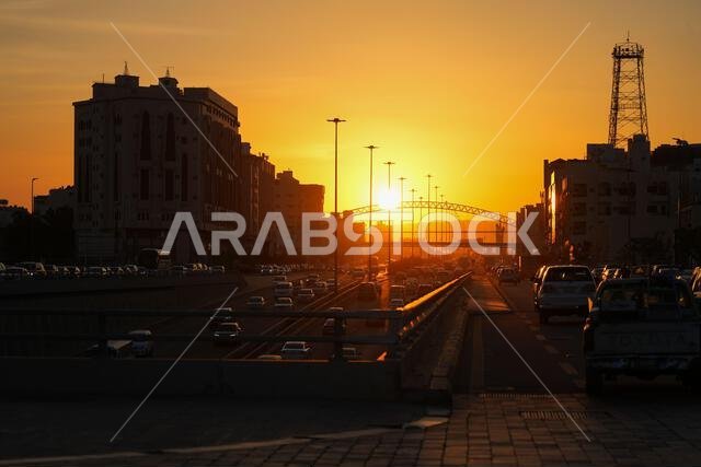 Urban traffic on Al Hijrah Road at sunset with pedestrian arch bridge in Madinah, Saudi Arabia