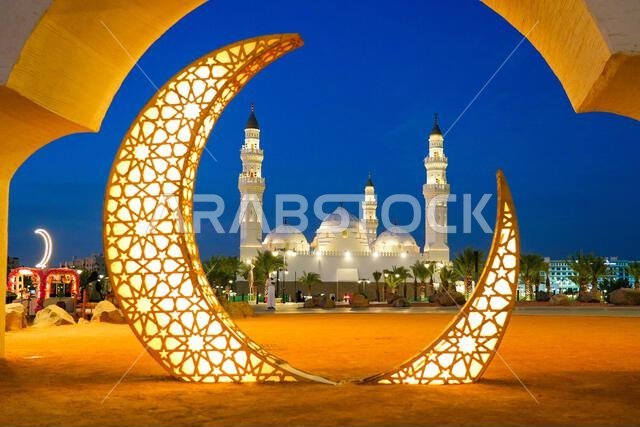 Historic white Quba Mosque framed by illuminated crescent moons at blue hour in Madinah, Saudi Arabia