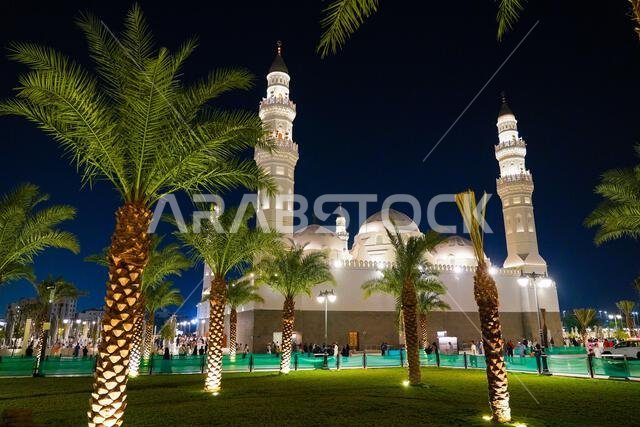 مسجد قباء الأبيض التاريخي وأشجار النخيل المضاءة ليلاً في المدينة المنورة، المملكة العربية السعودية