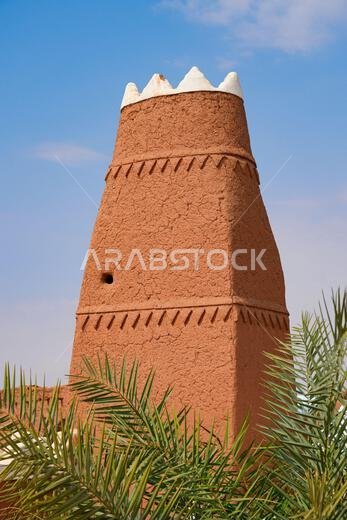 Mud brick minaret of Al-Faylaqia Mosque with white crenellations in Ushaiqer, Saudi Arabia