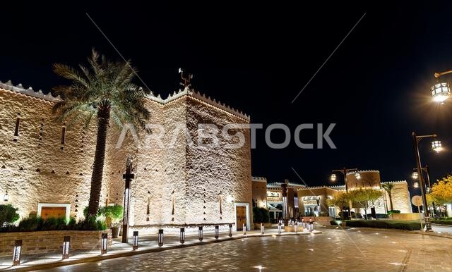 Beautifully illuminated Najdi style architecture at Bujairi Terrace in the historic district of Diriyah, Saudi Arabia at night.