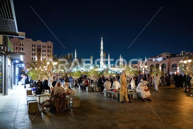 Pilgrims resting at night on Al Manakha Square with the illuminated minarets of the Prophet Mosque in Madinah, Saudi Arabia