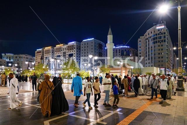 حجاج يسيرون ليلاً في الساحة العامة خارج مسجد علي بن أبي طالب في المدينة المنورة، المملكة العربية السعودية