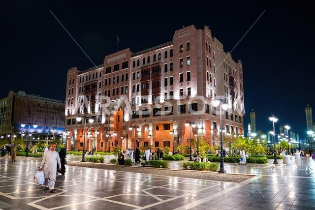 حجاج يسيرون ليلاً في ساحة المناخة المضاءة بالقرب من الفنادق الفاخرة في المدينة المنورة، المملكة العربية السعودية