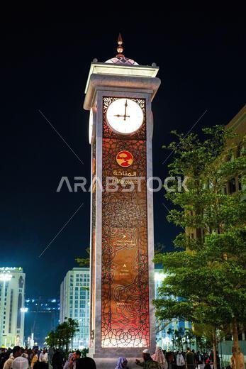 The illuminated Al Manakha clock tower and directional signpost at night in Madinah, Saudi Arabia