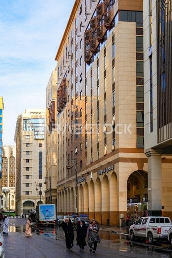 حجاج يسيرون على شارع مبلل خارج فنادق فاخرة حديثة بالقرب من ساحة الحرم في المدينة المنورة، المملكة العربية السعودية