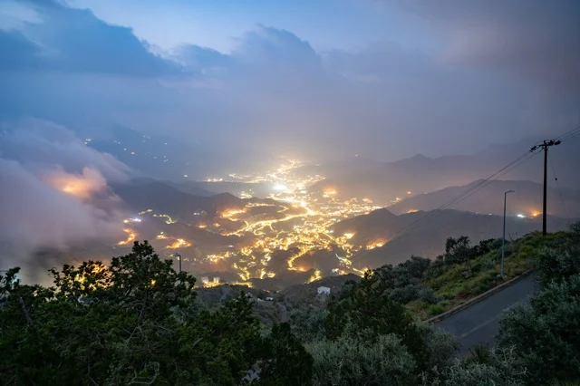 Aerial view of the city of Asir from above the mountains, the green mountainous nature in Abha, foggy winter atmosphere at night, tourism in the Kingdom of Saudi Arabia.