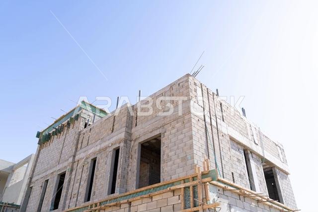منزل جديد قيد الإنشاء في الرياض، المملكة العربية السعودية، يظهر جدراناً إسمنتية، وهيكلاً غير مكتمل، ومراحل بناء مبكرة لعقار سكني.