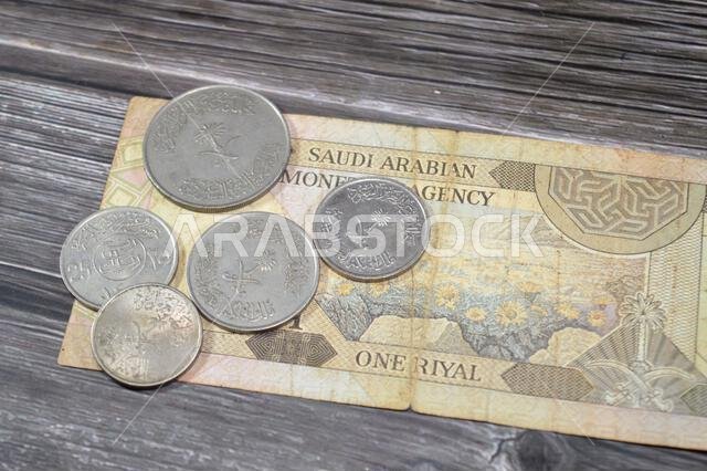 Old Saudi Arabian coins of different values on Saudi Arabia banknote bill, one 1 Riyal SAR, vintage retro, Riyals money exchange rate and economy stat