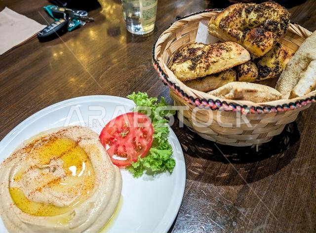 Traditional hummus topped with olive oil, served with a basket of fresh bread on a table at a local restaurant in Riyadh, Saudi Arabia