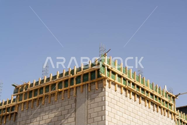 منزل جديد قيد الإنشاء في الرياض، المملكة العربية السعودية، يظهر جدراناً إسمنتية، وهيكلاً غير مكتمل، ومراحل بناء مبكرة لعقار سكني.