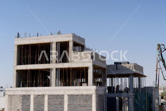 منزل جديد قيد الإنشاء في الرياض، المملكة العربية السعودية، يظهر جدراناً إسمنتية، وهيكلاً غير مكتمل، ومراحل بناء مبكرة لعقار سكني.