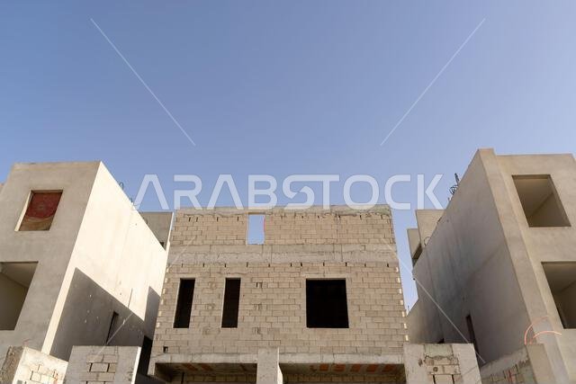 منزل جديد قيد الإنشاء في الرياض، المملكة العربية السعودية، يظهر جدراناً إسمنتية، وهيكلاً غير مكتمل، ومراحل بناء مبكرة لعقار سكني.