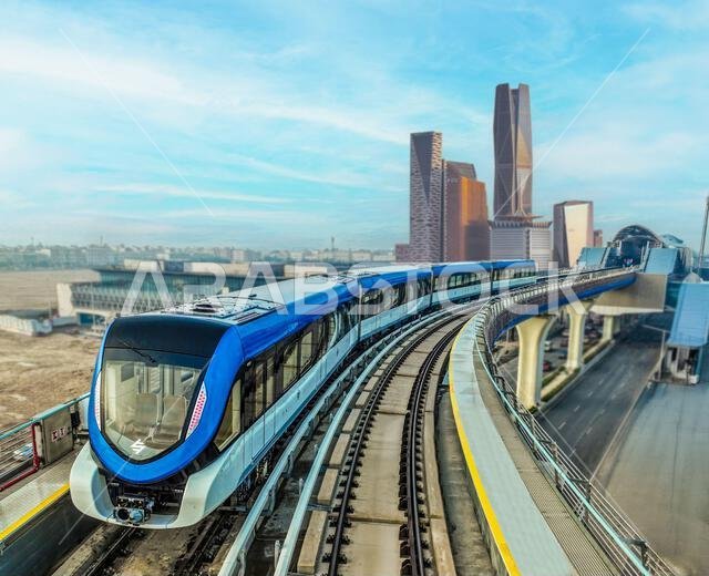 قطار الخط الأزرق لمترو الرياض يسير على مساره مع أفق الحي المالي للملك عبد الله في الخلفية، الرياض، المملكة العربية السعودية.