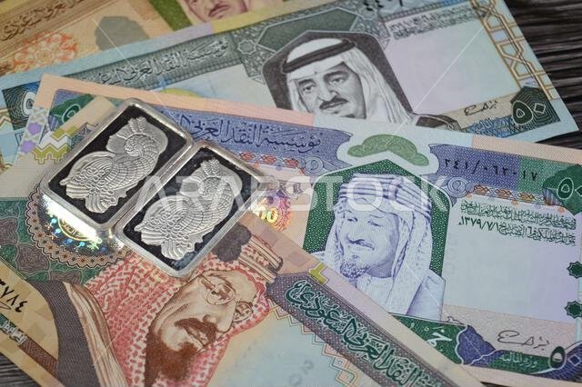 Old Saudi Arabian money banknotes of riyals and Silver precious metal ounce bars of pure silver, The price of silver is driven by speculation, supply