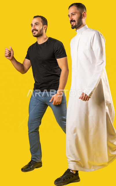 بورتريه لرجلان عربيان خليجيان سعوديان مبتسمان، صديقان يسيران معاً في نزهة ممتعة لإحدى الأماكن الترفيهية، صداقات وتعارف، علاقات إجتماعية، قضاء أوقات ممتعة، صورة الجسم بالطول الكامل، خلفية صفراء