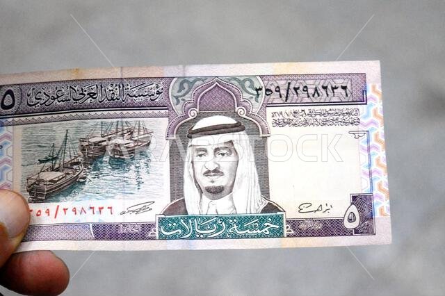 the obverse side of 5 SAR five Saudi Arabian riyals cash money banknote bill, features a portrait of king Fahd Bin AbdulAziz Al Saud and Dhows at lef the obverse side of 5 SAR five Saudi Arabian riyals cash money banknote bill, features a portrait of king Fahd Bin AbdulAziz Al Saud and Dhows at lef