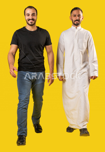 Portrait of two smiling Saudi Arabian Gulf men, two friends walking together on an enjoyable outing to a recreational place, friendships and acquaintances, social relationships, spending fun times, full length body image, yellow background