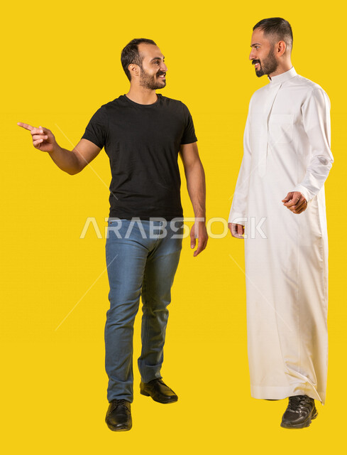 بورتريه لرجلان عربيان خليجيان سعوديان مبتسمان، صديقان يسيران معاً في نزهة ممتعة لإحدى الأماكن الترفيهية، صداقات وتعارف، علاقات إجتماعية، قضاء أوقات ممتعة، صورة الجسم بالطول الكامل، خلفية صفراء
