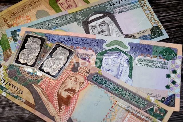 Old Saudi Arabian money banknotes of riyals and Silver precious metal ounce bars of pure silver, The price of silver is driven by speculation, supply