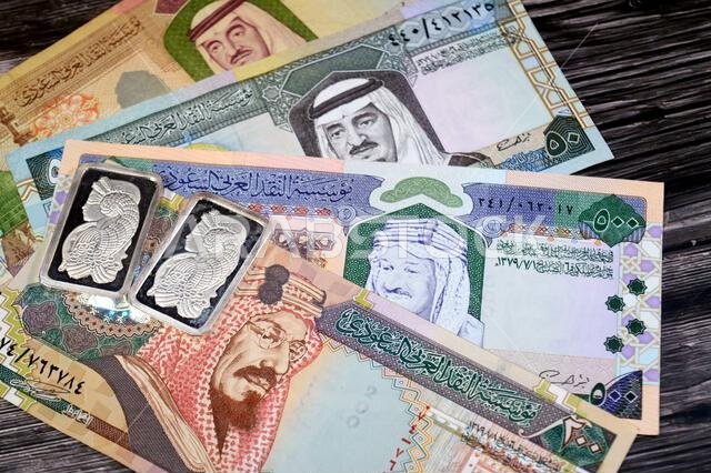 Old Saudi Arabian money banknotes of riyals and Silver precious metal ounce bars of pure silver, The price of silver is driven by speculation, supply
