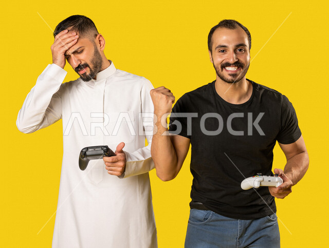 بورتريه لرجلان عربيان خليجيان سعوديان يحملان عصا التحكم، صديقان يستمتعان بلعب العاب الفيديو، اللعب والترفيه، التحدي والمغامرة، مفهوم الفوز والخسارة، تقنيات وألعاب، ايماءات وجه ويدين تدل على الفوز والانتصار، خلفية صفراء