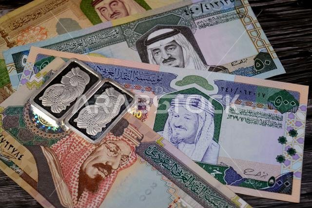 Old Saudi Arabian money banknotes of riyals and Silver precious metal ounce bars of pure silver, The price of silver is driven by speculation, supply