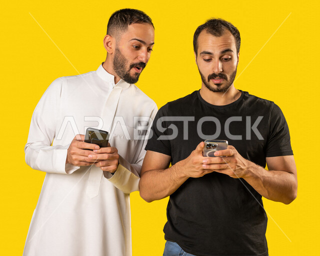 بورتريه لرجلان عربيان خليجيان سعوديان يستخدمان الهاتف المحمول، استخدام البرامج والتطبيقات الالكترونية، النظر خلسة للهاتف الاخر، المراقبة والتطفل، التلصص على الهواتف الشخصية، تصفح المواقع الالكترونية، ادمان الانترنت، خلفية صفراء