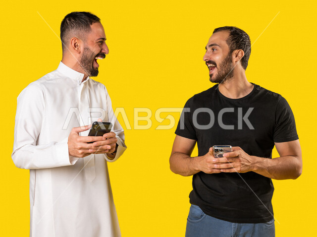 بورتريه لرجلان عربيان خليجيان سعوديان يستخدمان الهاتف المحمول، استخدام البرامج والتطبيقات الالكترونية، التسوق الالكتروني، التواصل الاجتماعي، تصفح المواقع الالكترونية، ادمان الانترنت، خلفية صفراء