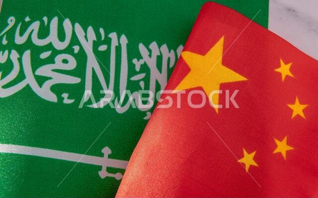 A close up of the national flag of Saudi Arabia next to the national flag of China. A Saudi Arabia, China relations concept.