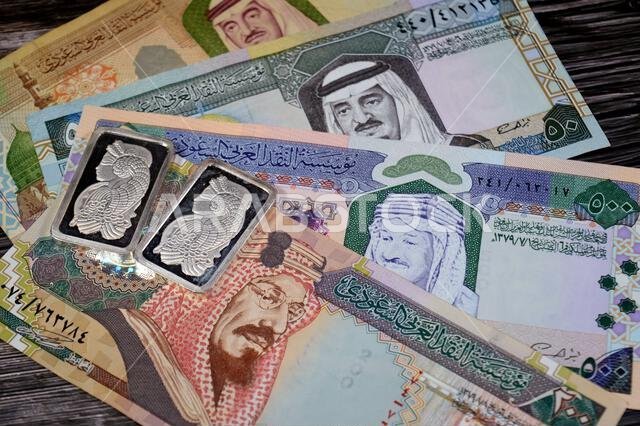 Old Saudi Arabian money banknotes of riyals and Silver precious metal ounce bars of pure silver, The price of silver is driven by speculation, supply
