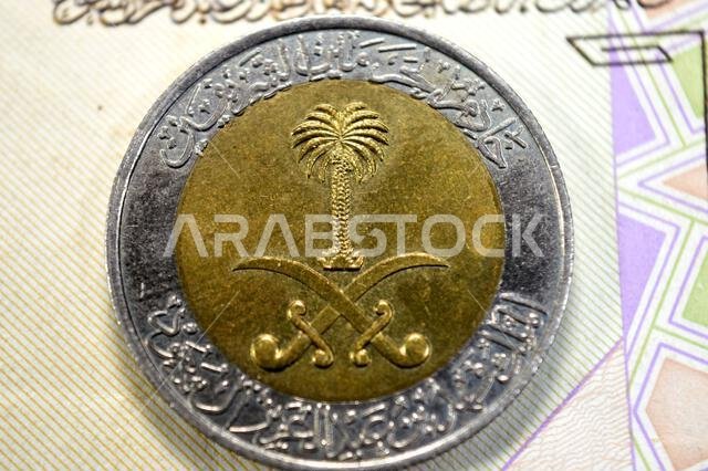 The obverse side of 1 SAR one Saudi Arabian Riyal coin features National emblem at the center, lettering around, Custodian of the Two Holy Mosques Kin