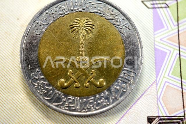 The obverse side of 1 SAR one Saudi Arabian Riyal coin features National emblem at the center, lettering around, Custodian of the Two Holy Mosques Kin
