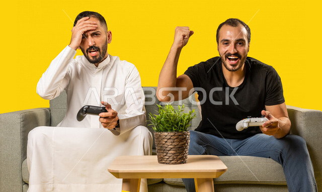 بورتريه لرجلان عربيان خليجيان سعوديان يحملان عصا التحكم، صديقان يستمتعان بلعب العاب الفيديو، اللعب والترفيه، التحدي والمغامرة، مفهوم الفوز والخسارة، تقنيات وألعاب، ايماءات وجه ويدين تدل على الفوز والانتصار، خلفية صفراء