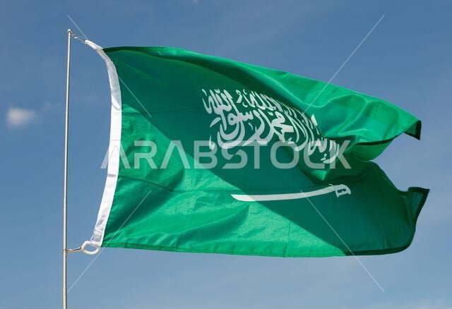 Flag of Saudi Arabia fluttering on flagpole against blue sky Flag of Saudi Arabia fluttering on flagpole against blue sky