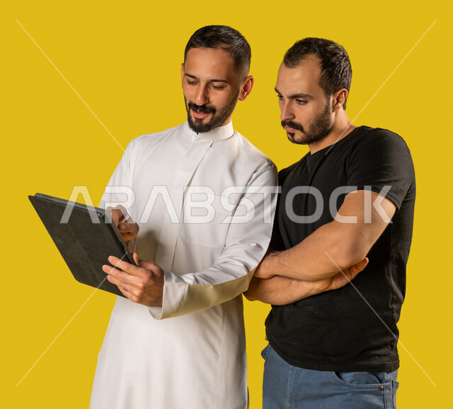 بورتريه لرجلان عربيان خليجيان سعوديان يقف بجانبها موظف يحمل بيده تابليت، التناقش بامور العمل، فريق عمل خليجي سعودي، مناقشة وتنظيم الاعمال، تحقيق اهداف العمل، خلفية صفراء