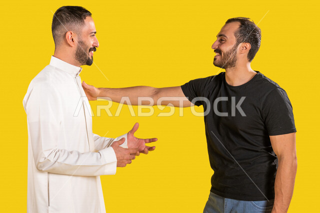 بورتريه لرجلان عربيان خليجيان سعوديان، العلاقات الأخوية المترابطة، علاقات اجتماعية، تعارف وصداقات، صديق يضع يده على كتف صديقه، إيماءات وجه ويدين تدل على السعادة الشديدة، خلفية صفراء