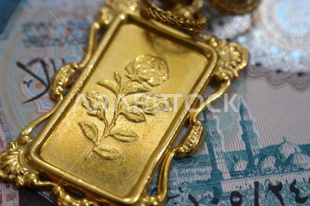 صورة مقرّبة لأوراق نقدية من الريال السعودي وزخارف زهرية على قلادة من الذهب عيار 24 قيراطًا، ذهب نقي عيار 999.9، للاستثمار أو الادخار