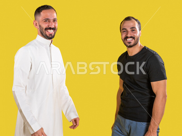 Portrait of two Saudi Arabian Gulf men, interconnected brotherly relations, social relations, acquaintance and friendships, different facial and hand gestures indicating happiness, standing with confidence, yellow background