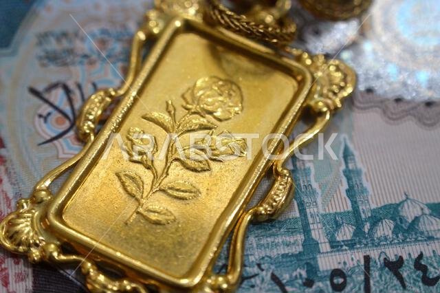 صورة مقرّبة لأوراق نقدية من الريال السعودي وزخارف زهرية على قلادة من الذهب عيار 24 قيراطًا، ذهب نقي عيار 999.9، للاستثمار أو الادخار
