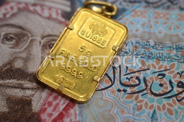Cairo, Egypt, October 29 2025: A closeup view of SAR Saudi Arabian riyals cash money banknote and PAMP Suisse gold bar pendant, 24K Gold Bar 5 Grams,