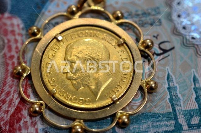 SAR Saudi Arabian riyals money and obverse side of King George V gold sovereign coin, features a left-facing portrait of King George V, sovereigns are