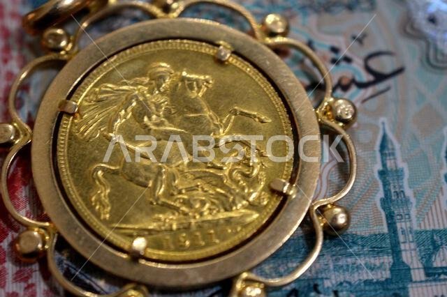 عملة الريال السعودي، والوجه الخلفي لعملة الملك جورج الخامس الذهبية، يتميز بصورة القديس جورج والتنين الكلاسيكية، والسيادات هي