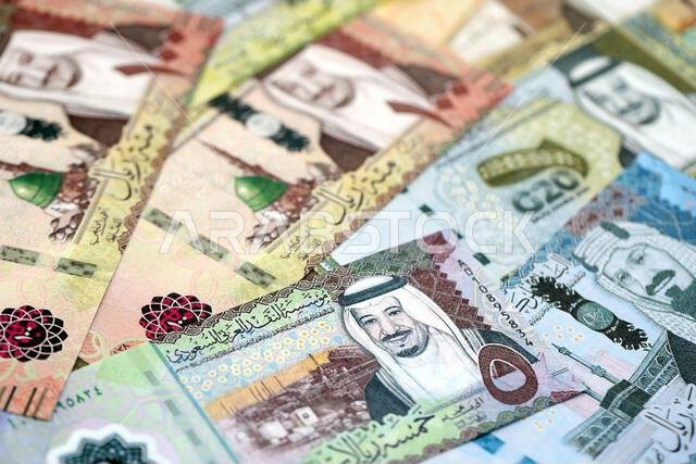 Saudi Arabia riyal money bills banknotes lies in big pile on table close up. Concept of finances and business in Saudi Arabia