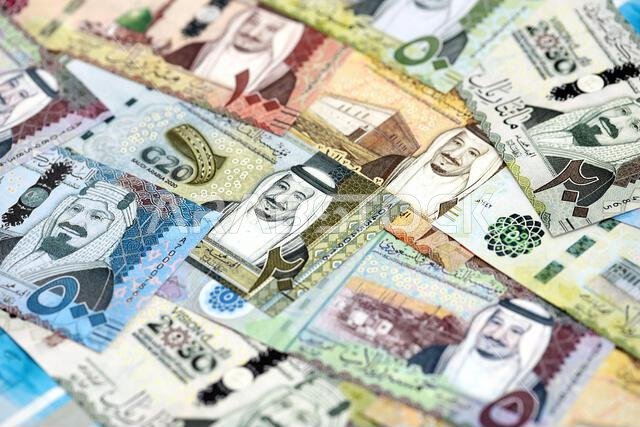 Saudi Arabia riyal money bills banknotes lies in big pile on table close up. Concept of finances and business in Saudi Arabia
