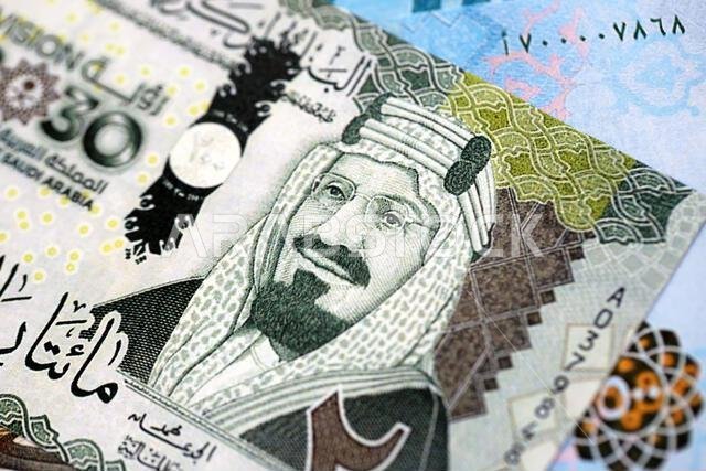 أوراق نقدية من الريال السعودي مكدسة في كومة كبيرة على طاولة، صورة مقرّبة. مفهوم التمويل والأعمال في المملكة العربية السعودية