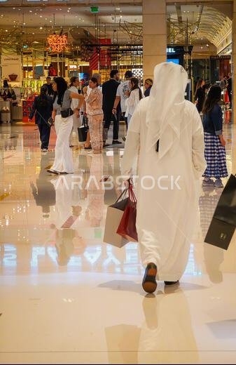 11 30 2025 - دبي، الإمارات العربية المتحدة. صورة من الخلف لرجال إماراتيين يرتدون الكندورة والثوب ويحملون أكياس التسوق داخل دبي مول