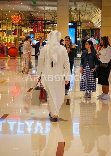 11 30 2025 - دبي، الإمارات العربية المتحدة. صورة من الخلف لرجال إماراتيين يرتدون الكندورة والثوب ويحملون أكياس التسوق داخل دبي مول