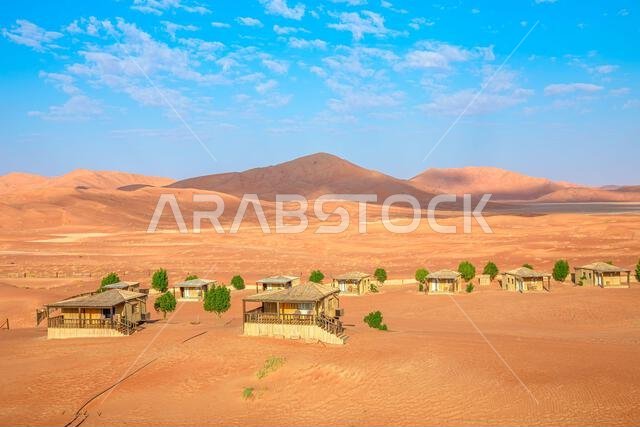 أكواخ تقليدية تقف وسط الكثبان الرملية الحمراء الشاسعة في صحراء الربع الخالي، تعكس العزلة والمغامرة في ثمريت، ظفار، عمان